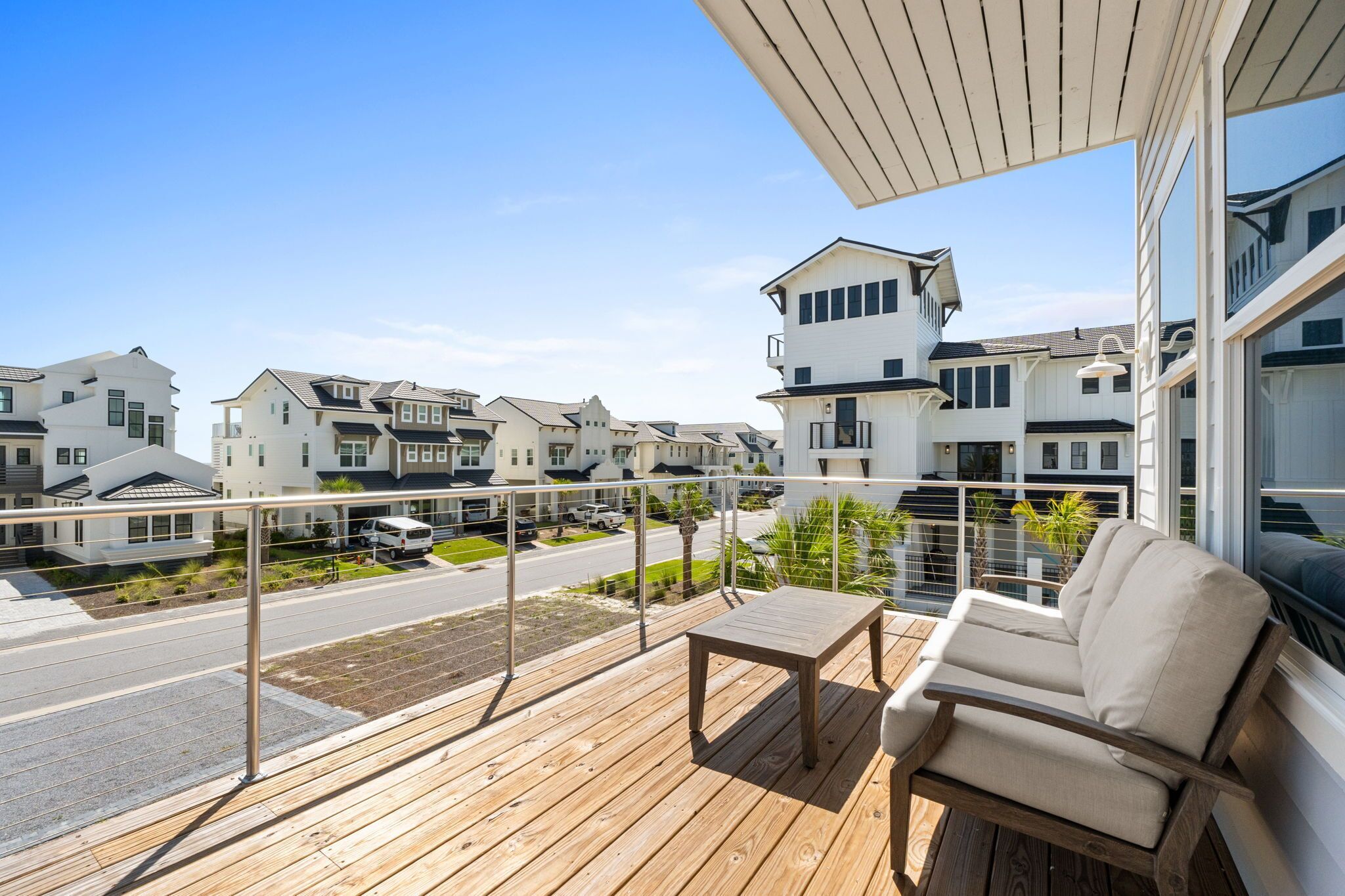 A wooden deck with a table and chairs, overlooking a street with modern houses.