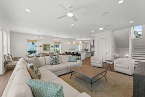 A spacious living room with a large sofa, a coffee table, and a dining area with chairs. There is a kitchen in the background with modern appliances. - Gulfstone: Gulf Front New Build, Private Pool, Pet Friendly, Sugar Sands Communi (Mexico Beach)