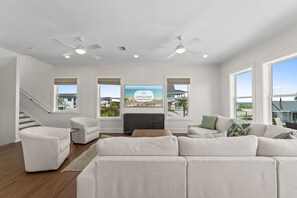 Ein geräumiges Wohnzimmer mit einer Eckcouch, einem Kamin und großen Fenstern mit Blick auf den Strand.