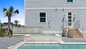 Zwembad met stenen rand, houten terras en trap naar een gebouw met horizontale bekleding.