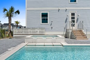 A swimming pool with a stone edge, a wooden deck, and a staircase leading to a building with horizontal siding. - Gulfstone: Gulf Front New Build, Private Pool, Pet Friendly, Sugar Sands Communi (Mexico Beach)