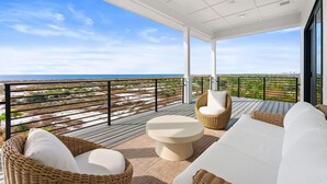 A balcony with wicker furniture, a round table, and a view of the beach and ocean. - Ocean Breeze: Unobstructed Views, Private Elevated Pool, Pet Friendly, Sleeps 19 (Mexico Beach)