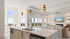A spacious kitchen with a large island, modern pendant lights, and a view of the ocean. - Ocean Breeze: Unobstructed Views, Private Elevated Pool, Pet Friendly, Sleeps 19 (Mexico Beach)