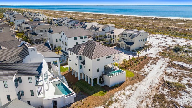 A coastal residential area with modern houses, a swimming pool, and a beach in the background. - Ocean Breeze: Unobstructed Views, Private Elevated Pool, Pet Friendly, Sleeps 19 (Mexico Beach)