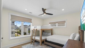 Ein Schlafzimmer mit Etagenbetten, einem Deckenventilator, einem Fenster mit Jalousien und Blick auf angrenzende Häuser.