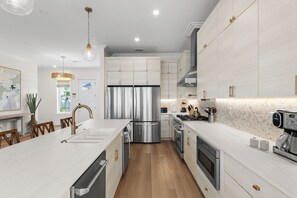 A modern kitchen with stainless steel appliances, wooden flooring, and a central island. - New Build, Private Pool, Pet Friendly, Sugar Sands Community (Mexico Beach)