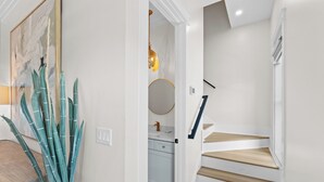 Eine Treppe mit Holzbodenstufen und weißen Wänden, die zu einem Raum mit Küchenzeile führt.