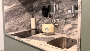Eine Küche mit Marmor-Spritzschutz, einem Spülbecken, einem Wasserkocher und Kochutensilien, die an der Wand hängen.