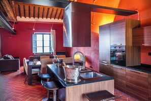 A modern kitchen with a central island, wooden cabinets, and a red accent wall. - Deluxe Apartment Borgo (Matraia)
