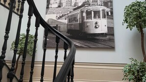 En trappa med svarta räcken, en väggmonterad lampa och ett inramat svartvitt fotografi av en spårvagn och en byggnad.