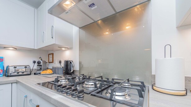 A modern kitchen with white cabinets, a stainless steel stove, and a glass backsplash. - Triple Driveway | Telford | Central | Long Stays (Telford)