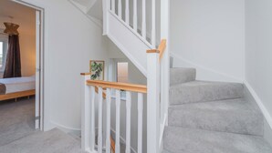 A staircase with white railings and wooden handrails, leading to a bedroom with a bed and a plant. - Triple Driveway | Telford | Central | Long Stays (Telford)