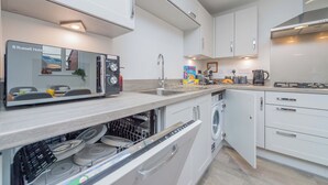 A modern kitchen with white cabinetry, a built-in dishwasher, a coffee maker, and a kettle. - Triple Driveway | Telford | Central | Long Stays (Telford)