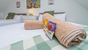 A neatly made bed with a rolled towel and a chocolate bar package, a green checkered bedspread, and a painting of horses on the wall. - Triple Driveway | Telford | Central | Long Stays (Telford)