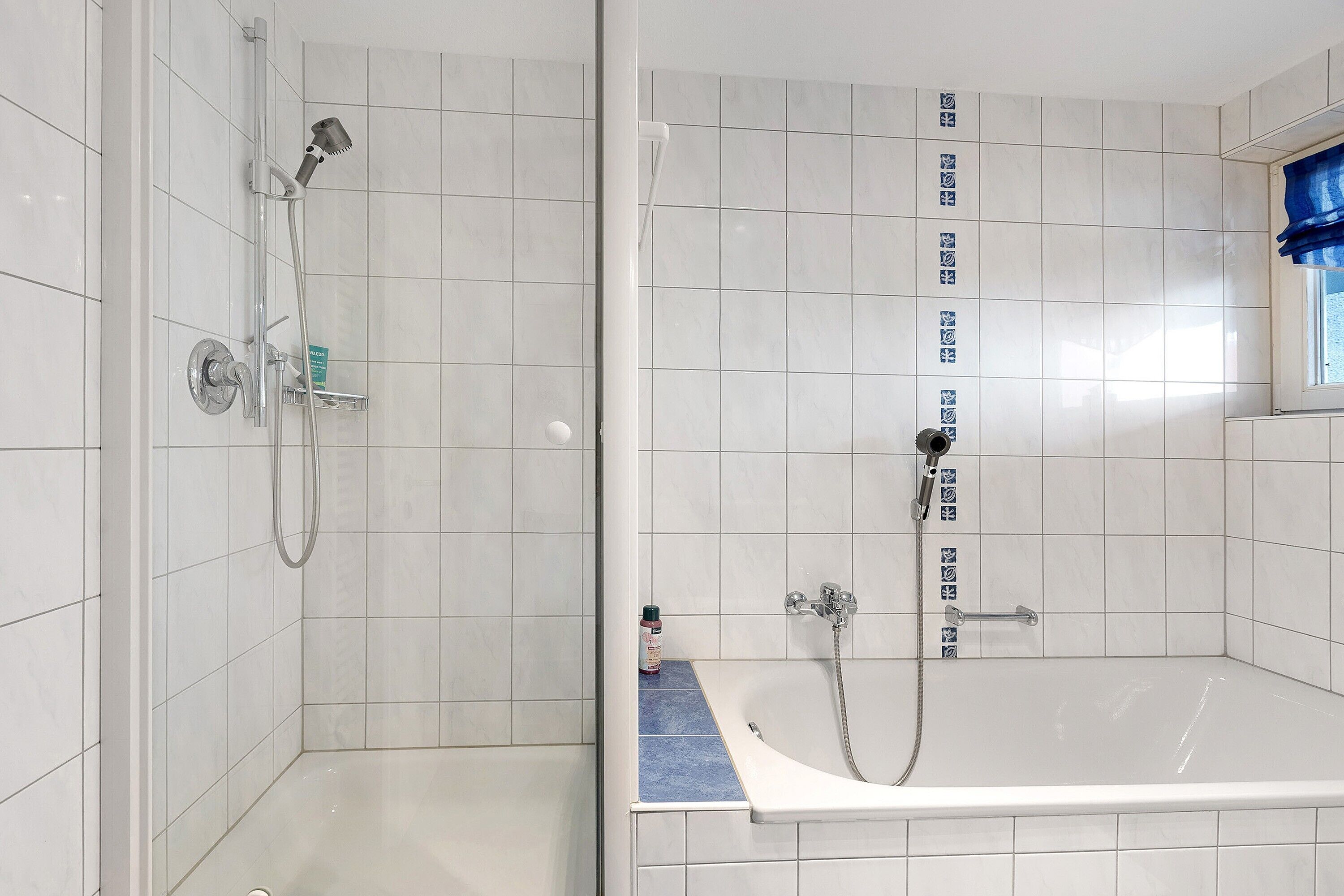 A bathroom with a shower, a bathtub, and a window with blue curtains.
