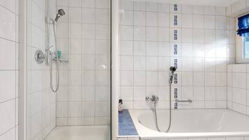 A bathroom with a shower, a bathtub, and a window with blue curtains.