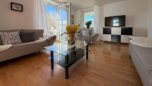 A modern living room with a glass coffee table, a sofa, a TV, and a view through the glass door. - Apartment Sieglinde with Private Terrace in Bad Dürrheim Öfingen (Bad Dürrheim)