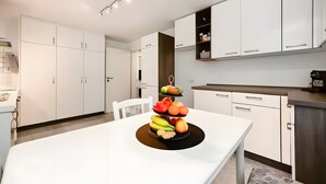 A modern kitchen with white cabinetry, a dining table with a fruit centerpiece, and a coffee machine. - Apartment Sieglinde with Private Terrace in Bad Dürrheim Öfingen (Bad Dürrheim)