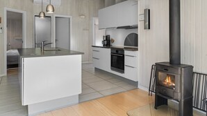 Een moderne keuken met een centraal eiland, een zwart houtgestookte kachel en witte kasten.