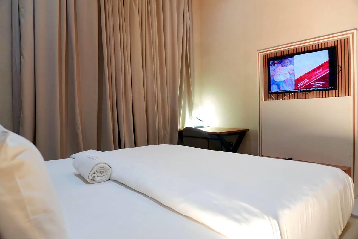 Une chambre d’hôtel avec un lit bien fait, un téléviseur fixé au mur et un bureau avec une chaise.