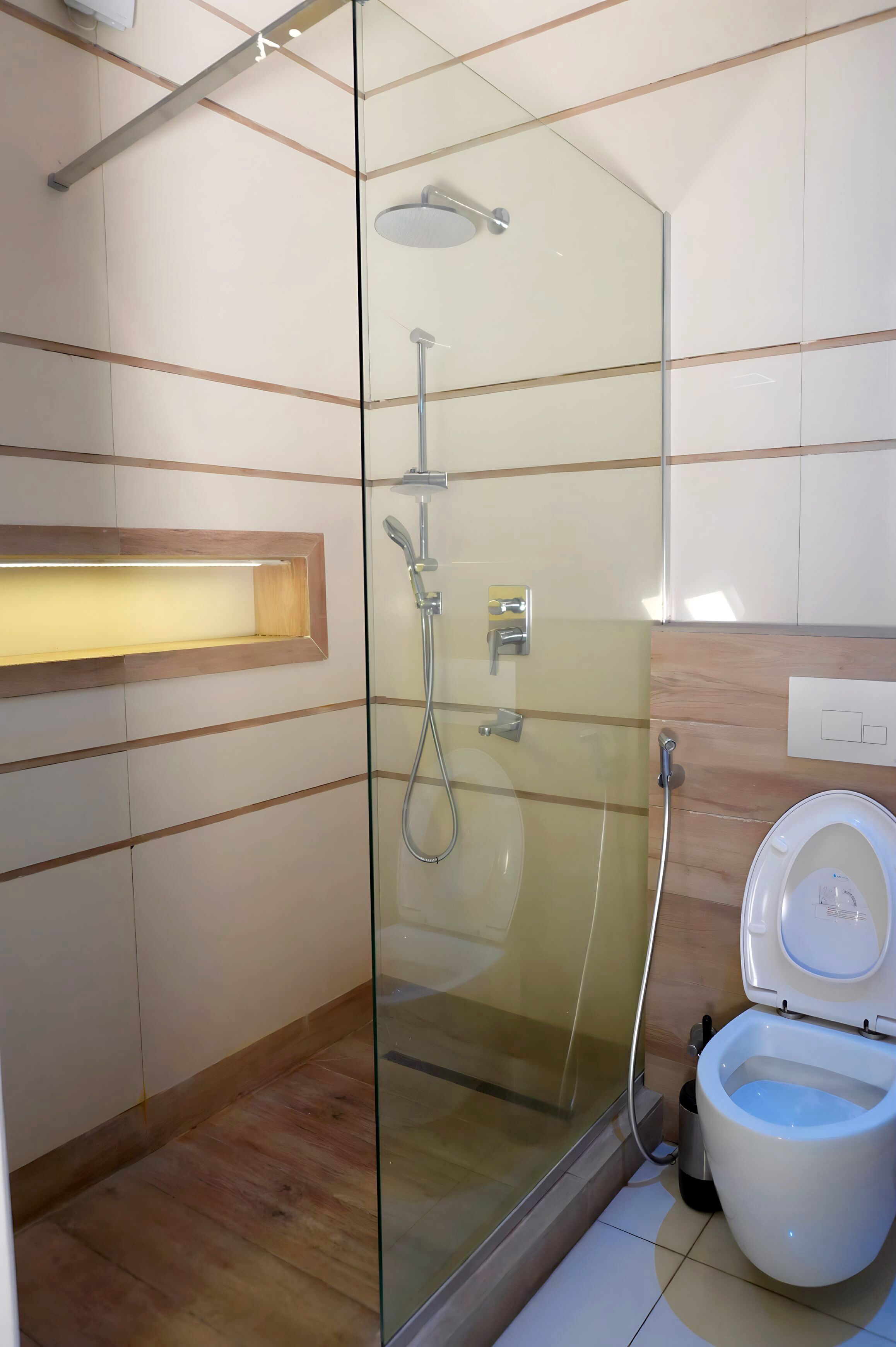 Une salle de bain moderne dotée d’une douche à parois de verre, de toilettes et d’un meuble-lavabo en bois avec un éclairage intégré.