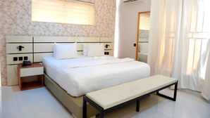 A neatly arranged bedroom with a bed, bedside tables, a bench, a window with blinds, and an air conditioning unit. - 2020 Apartment Guzape (Abuja)