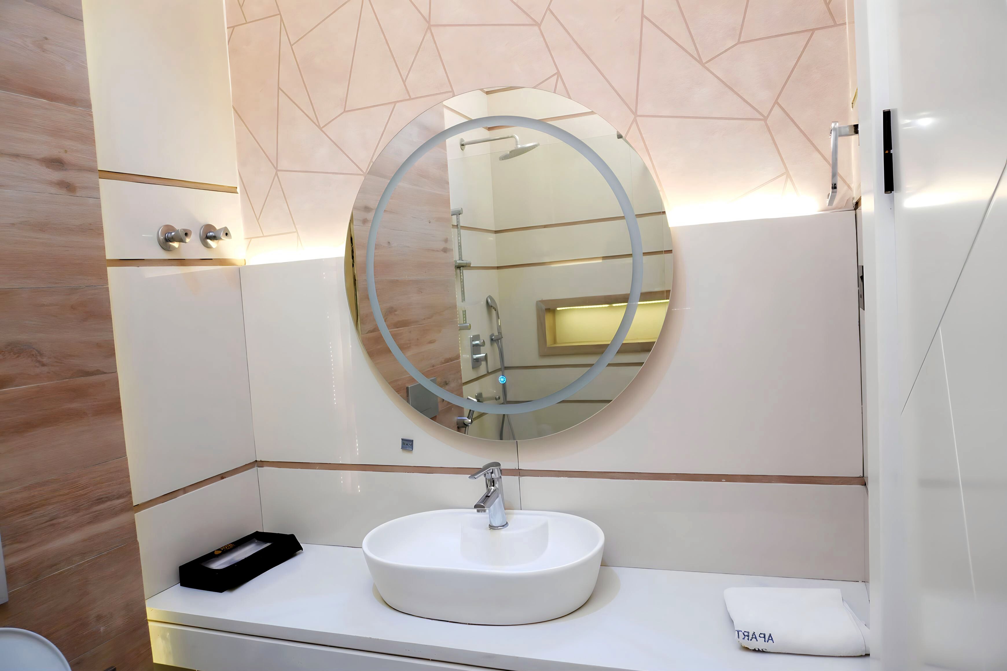 Une salle de bain moderne avec un miroir rond, un lavabo blanc et un porte-serviettes.