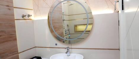 Une salle de bain moderne avec un miroir rond, un lavabo blanc et un porte-serviettes.