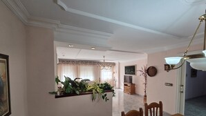 Ein Essbereich mit Holztisch und -stühlen, einer Pendelleuchte und einem an der Wand befestigten Regal mit Pflanzen.