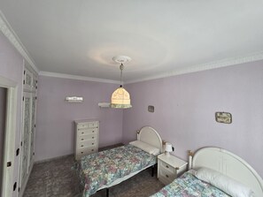 Un dormitori amb dos llits, un taulell, una làmpada penjant i una porta amb un panell decoratiu.