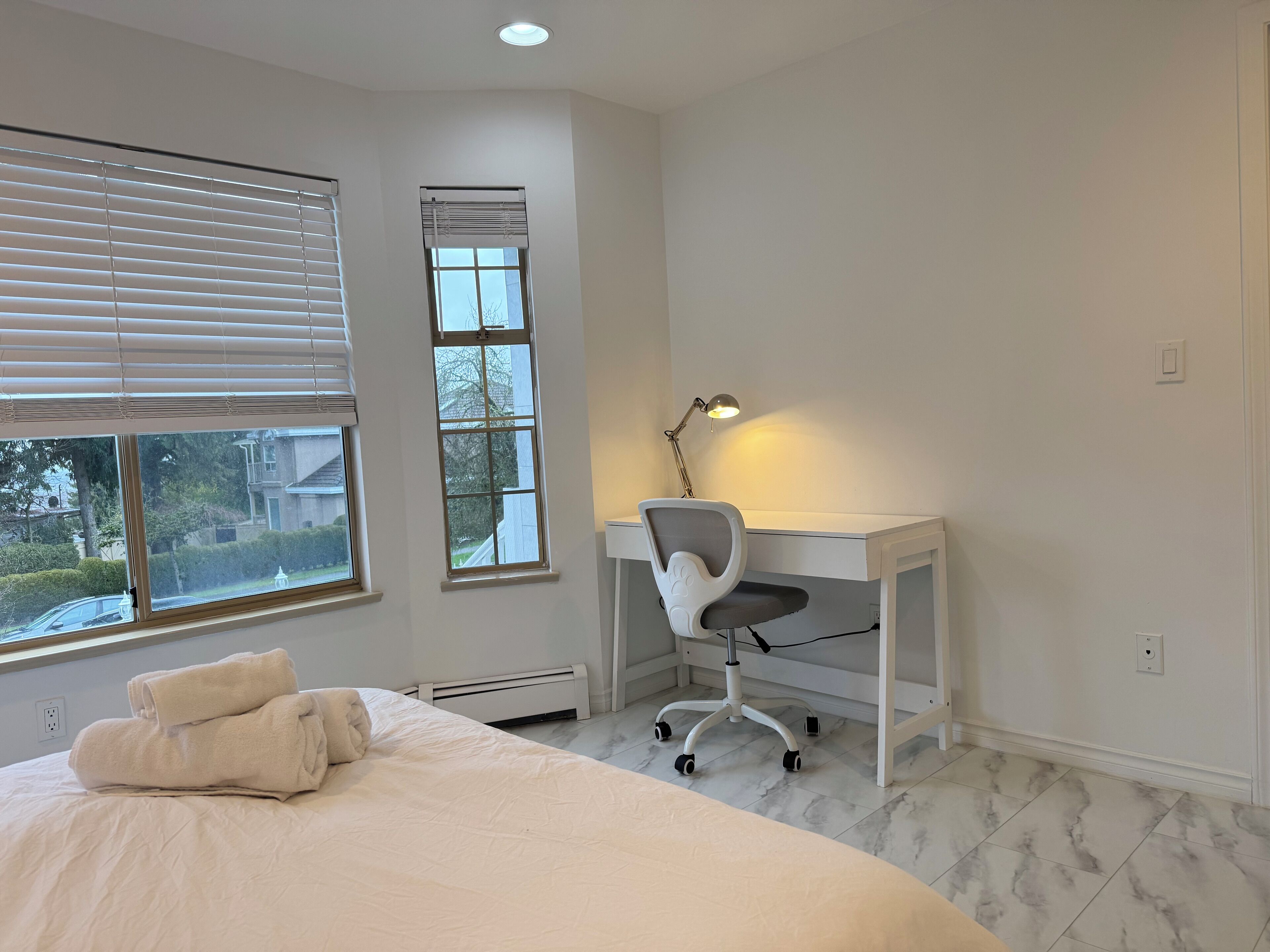 A bedroom with a bed, a desk, and two windows.