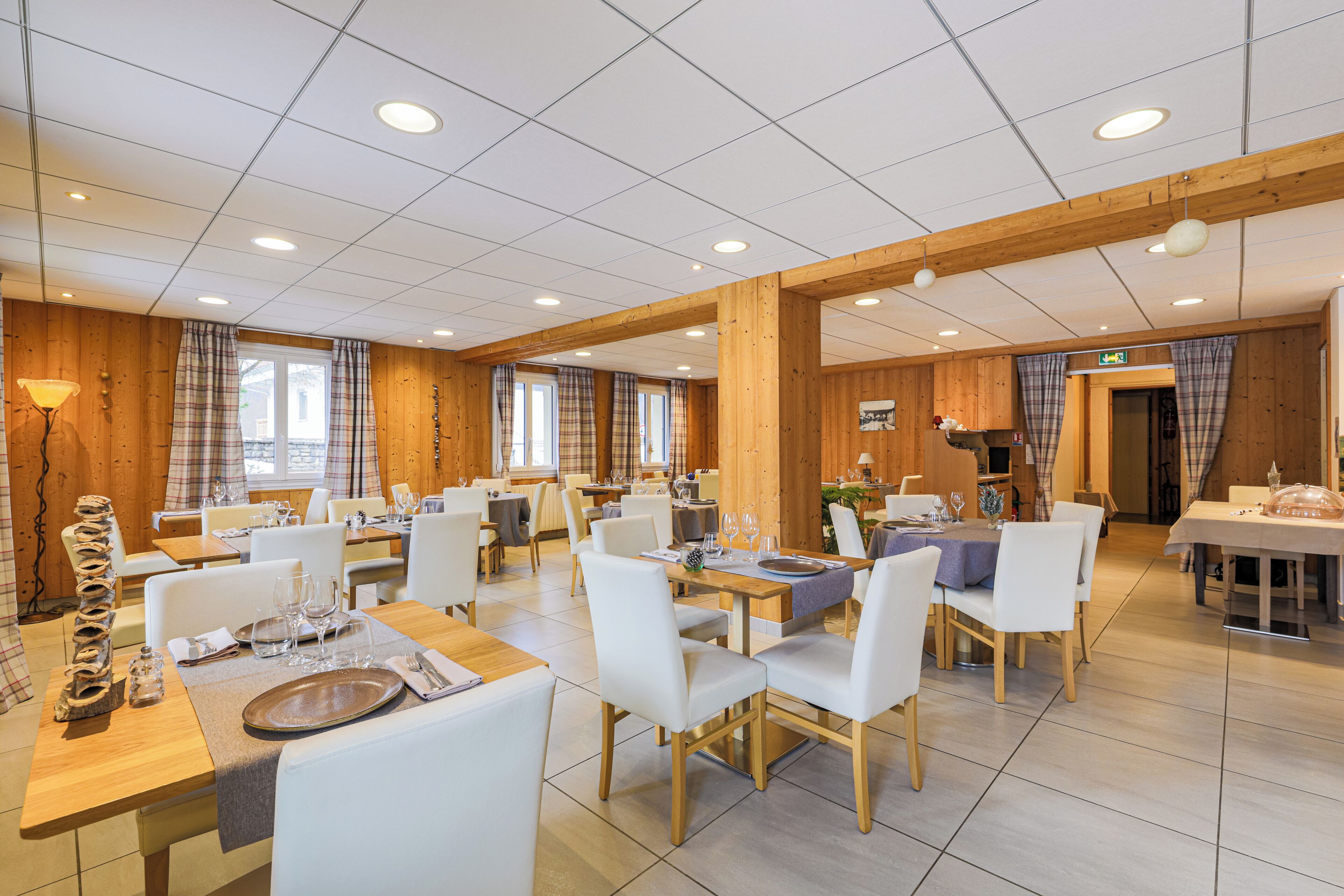 A spacious dining area with multiple tables and chairs, wooden paneling, and a clean, modern design.