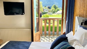 Ein Schlafzimmer mit Bett, einem an der Wand montierten Fernseher und einem Balkon mit Blick ins Freie.