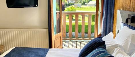 Un dormitorio con cama, televisor montado en la pared y balcón con vistas al exterior.
