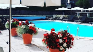Ein Poolbereich mit Liegestühlen, Sonnenschirmen und Kübelpflanzen.