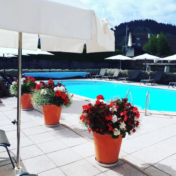 Ein Poolbereich mit Liegestühlen, Sonnenschirmen und Kübelpflanzen.