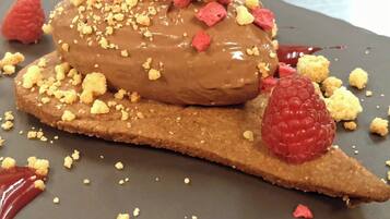 A dessert on a plate with a chocolate coating, crumbled topping, and raspberries.