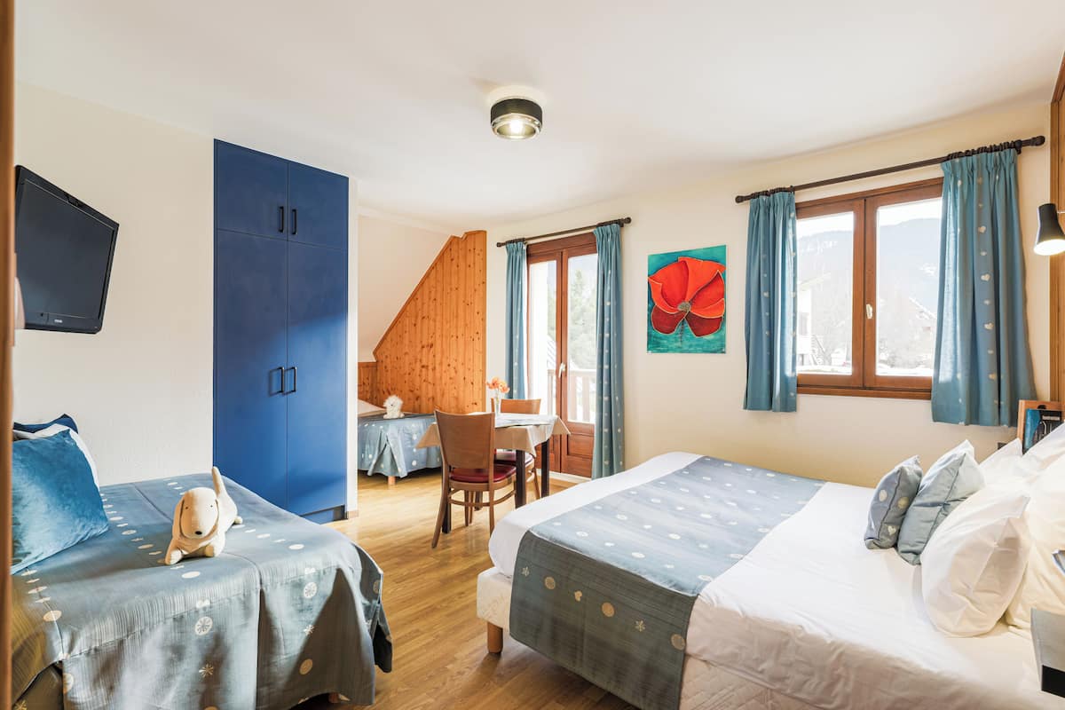 Un dormitorio con dos camas, una escalera de madera, un área de comedor y un amplio ventanal con cortinas.