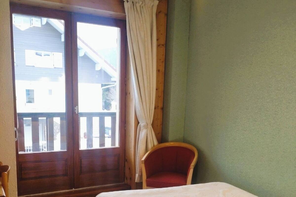 Un dormitorio con cama, una silla y una ventana con cortinas.