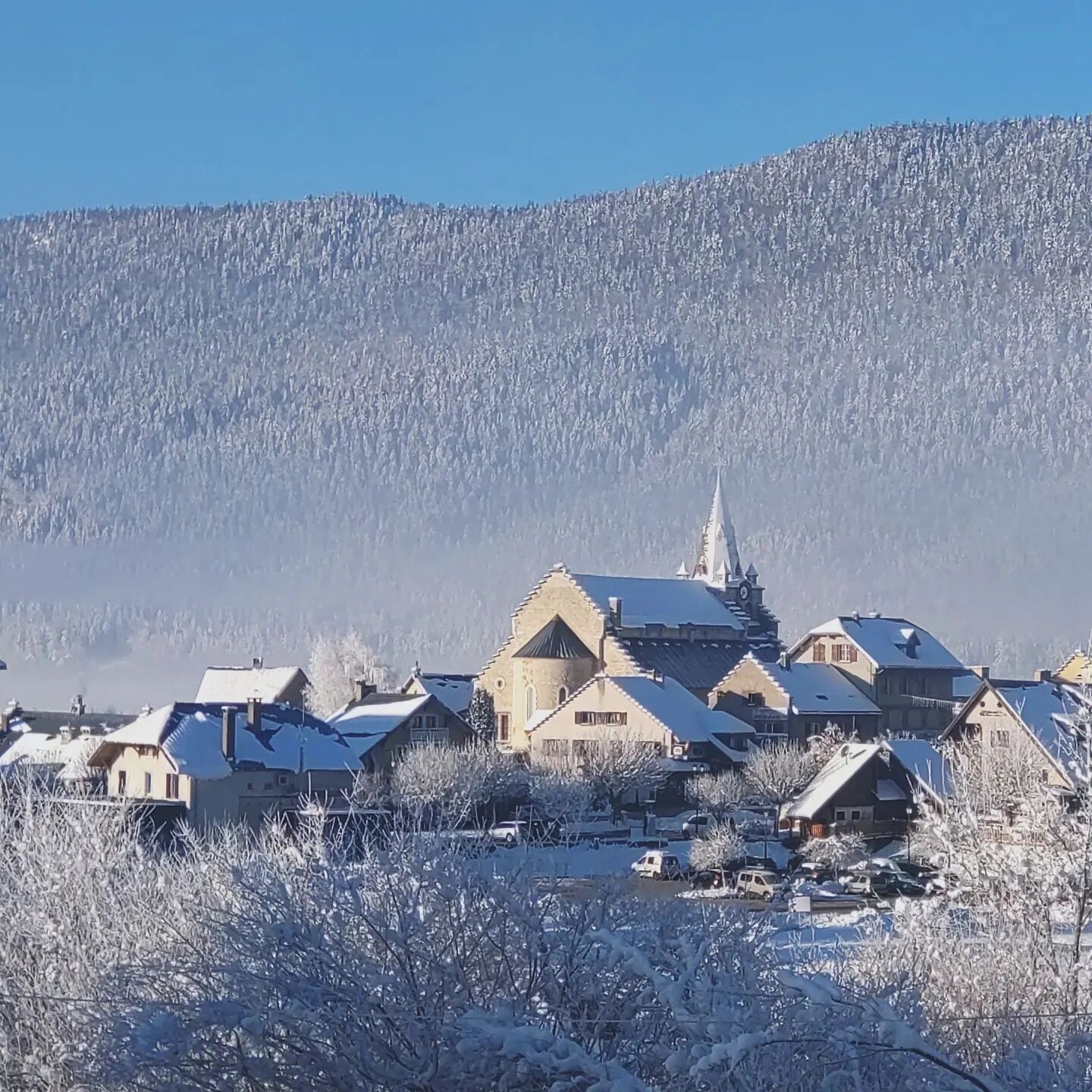 A snow-covered village with traditional architecture, including a church with a spire, surrounded by residential buildings.