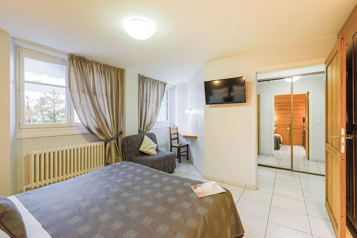 Un dormitorio con cama, una silla, un escritorio, un televisor y una puerta corredera que da a un baño.