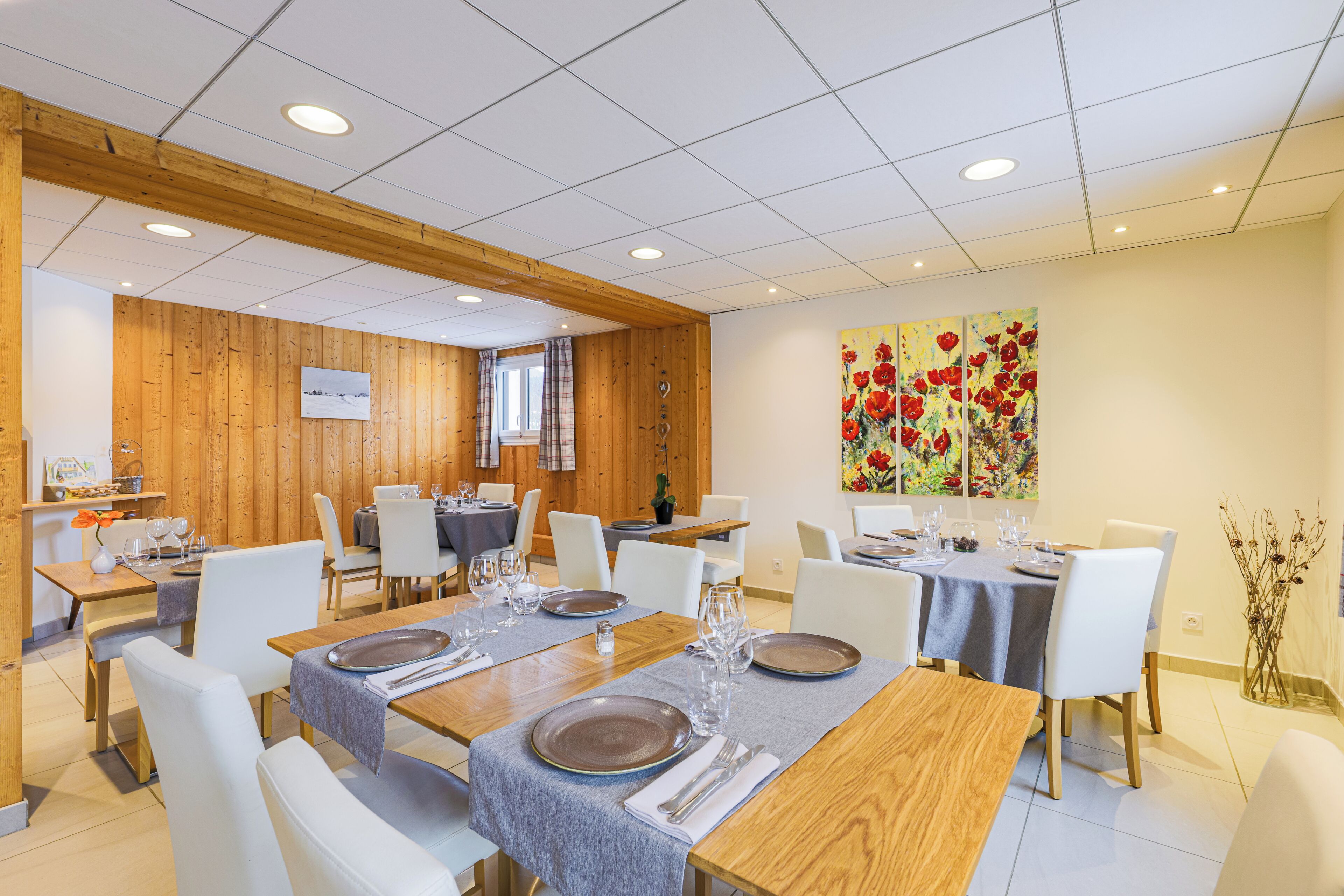 Un comedor con paredes de madera, sillas blancas y mesas dispuestas para cuatro comensales.
