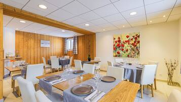 Un comedor con paredes de madera, sillas blancas y mesas dispuestas para cuatro comensales.