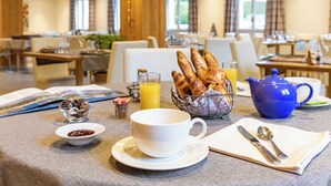 Ein Frühstückstisch mit Tasse, Croissants, Teekanne und einer kleinen Schale Marmelade.