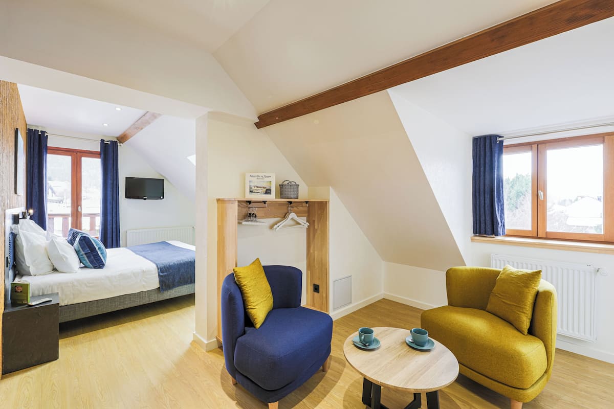 Una habitación moderna con una cama, un sillón azul, un sillón amarillo y una pequeña mesa con tazas.