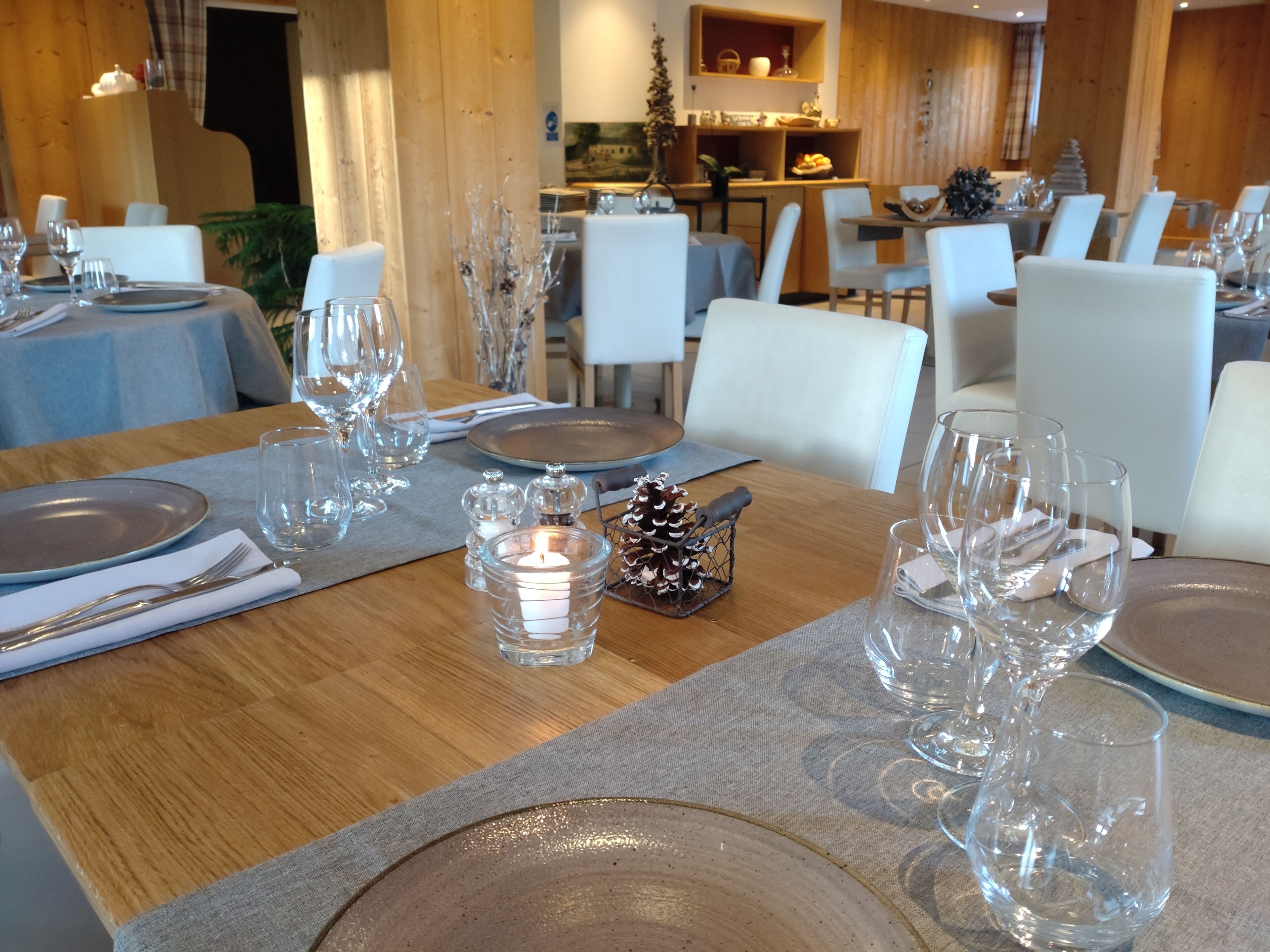 Un espace repas avec des tables mises pour le dîner, comprenant de la vaisselle transparente, des assiettes et des bougies.