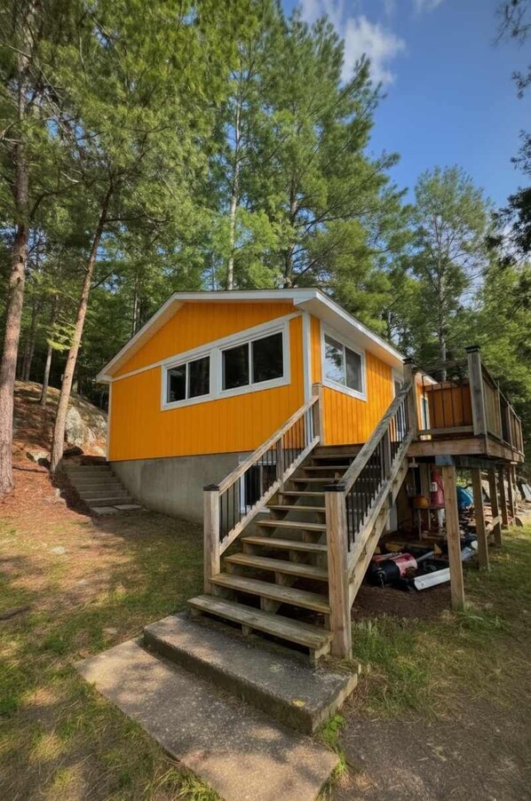 Une cabane jaune avec un escalier en bois menant à une terrasse.