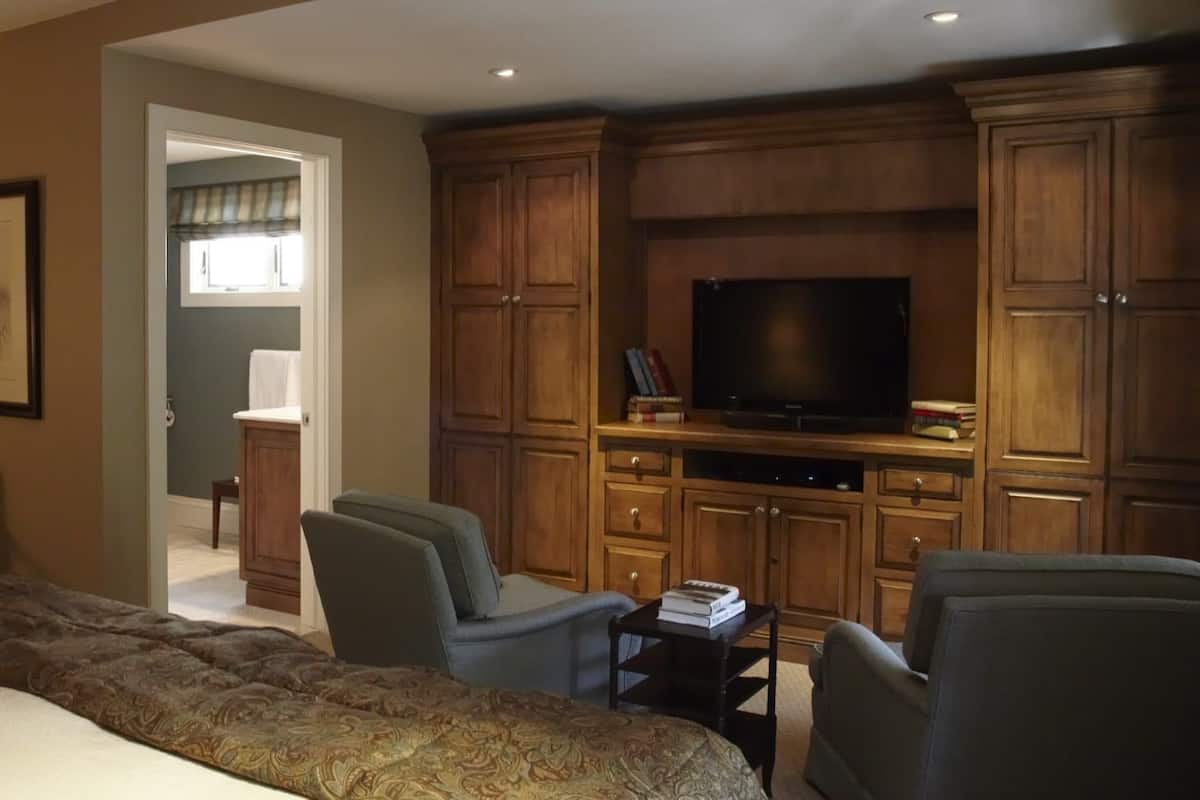 A hotel room with a bed, two armchairs, a TV, and wooden cabinets.