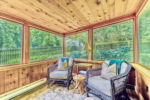 A wooden-paneled room with wicker furniture, large windows, and a view of a green landscape. - Black Bass Hotel (Lumberville)
