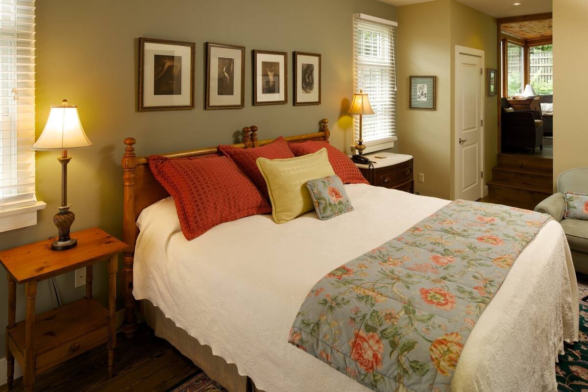 A bedroom with a large bed, two bedside tables, a nightstand, and a door leading to another room.